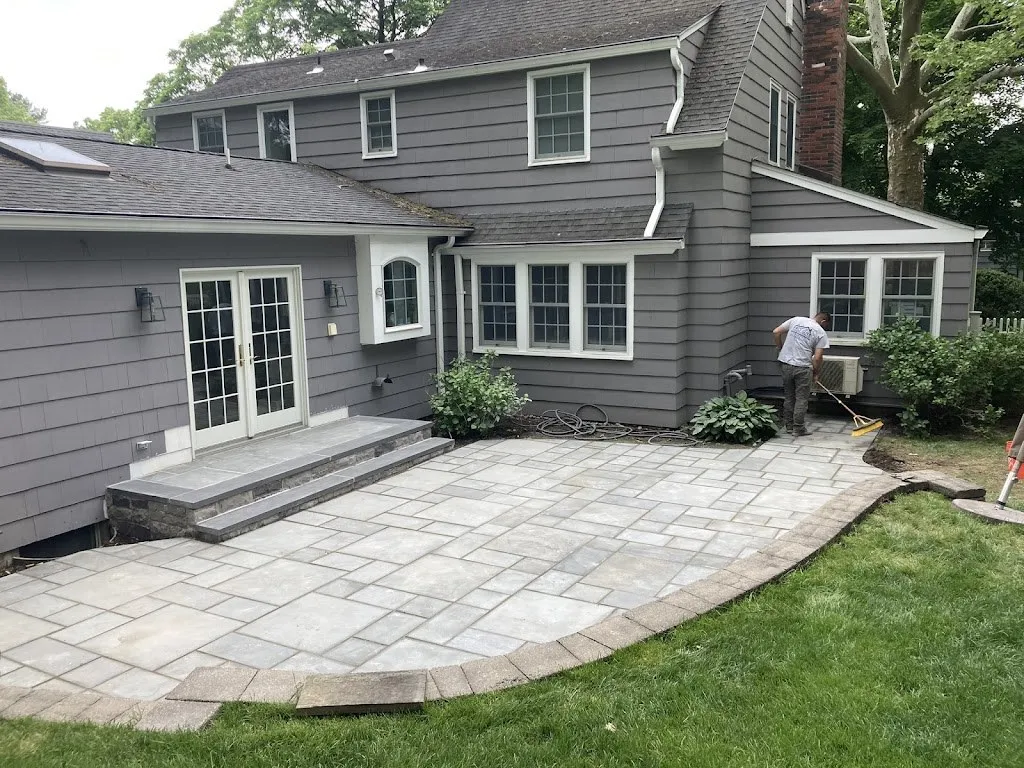 Gray paver patio with curved edge and stone step behind a gray house