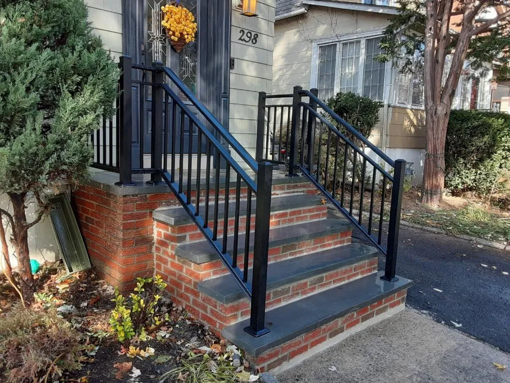 Rebuilt brick stoop with bluestone treads and new black railings beside a driveway
