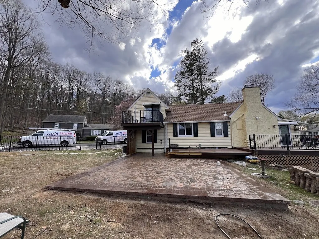 Wide view of a large paver patio behind a home with a deck