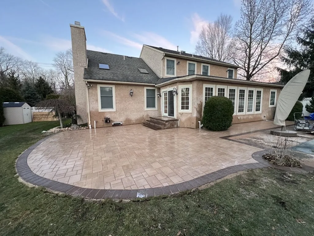 Circular tan paver patio with dark border wrapping a two-story home