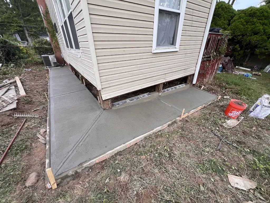 Freshly poured concrete walkway wrapping the corner of a house