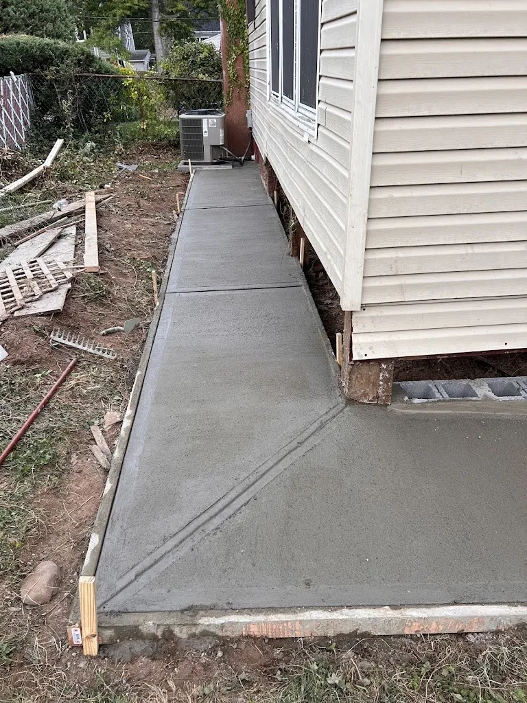 New concrete walkway poured along the foundation of a house with vinyl siding
