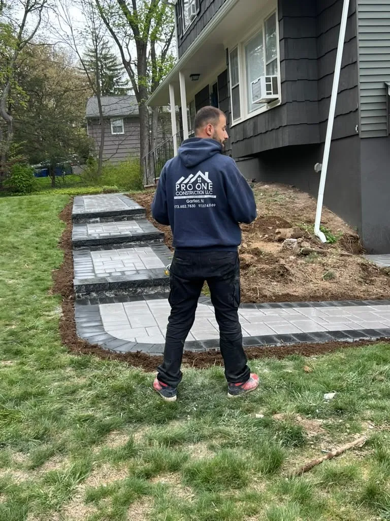 Pro One crew member beside a new gray paver walkway and steps at a dark colonial home