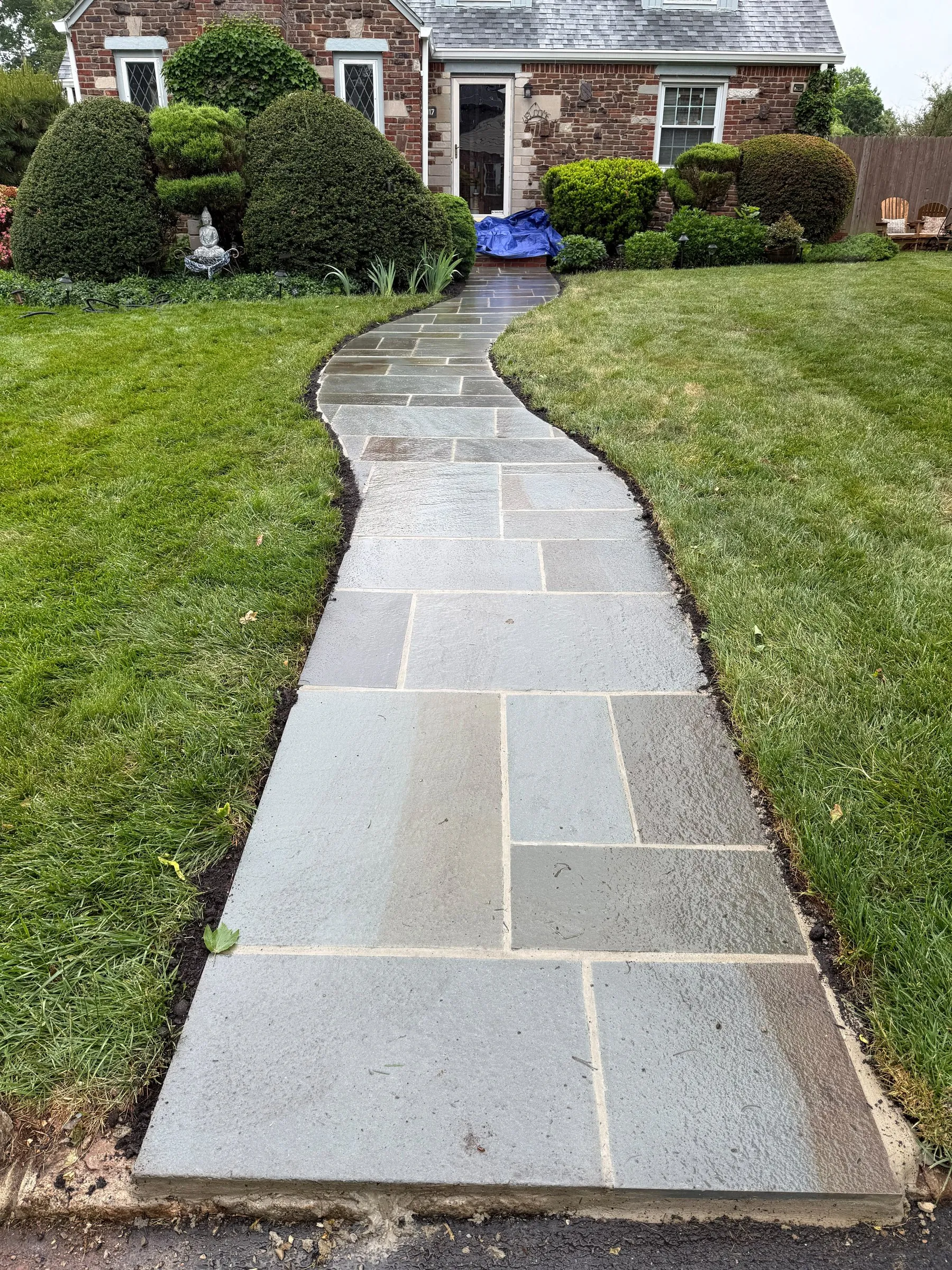 Curved bluestone front walkway through a lawn to a brick and stone cottage