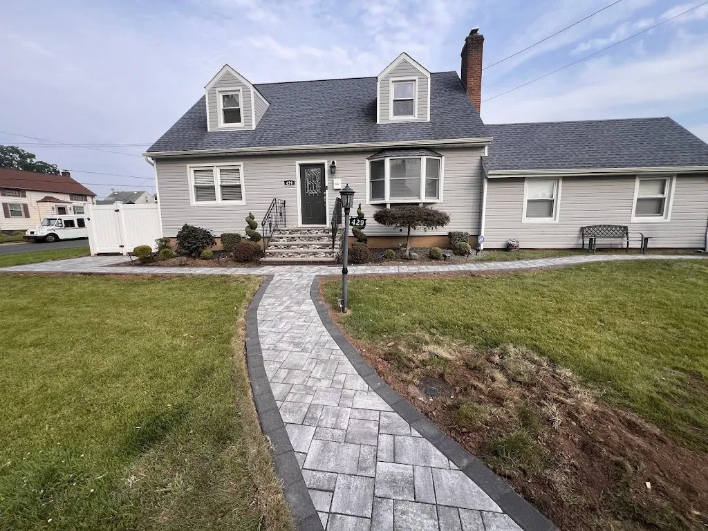 Curved gray paver walkway with dark border leading to a Cape Cod home