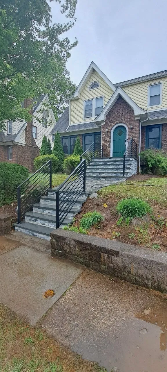 Front steps with black railings above a low stone retaining wall