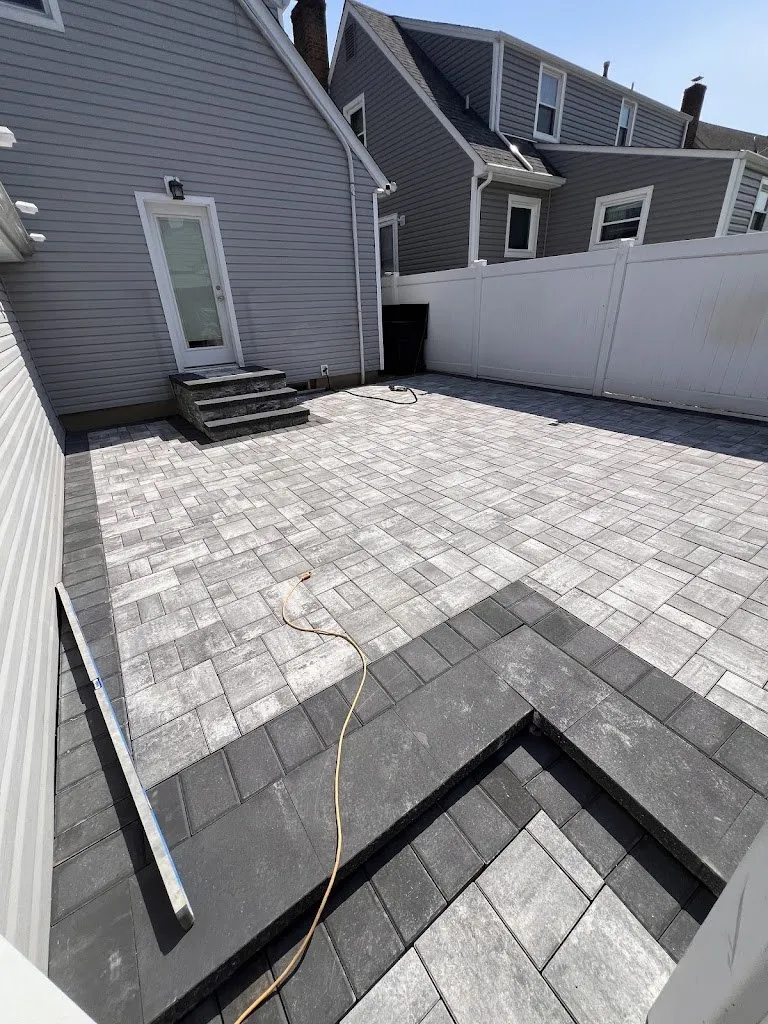 Gray paver patio with a charcoal border inlay along a fence