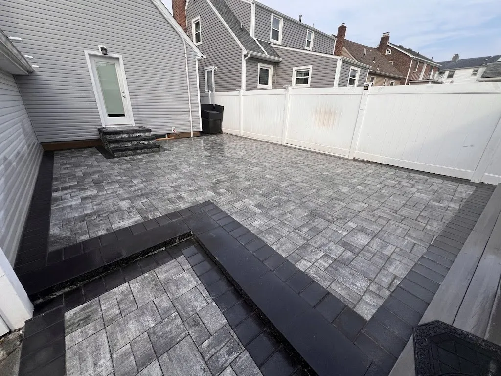 Gray paver patio with charcoal border inlay in a fenced yard