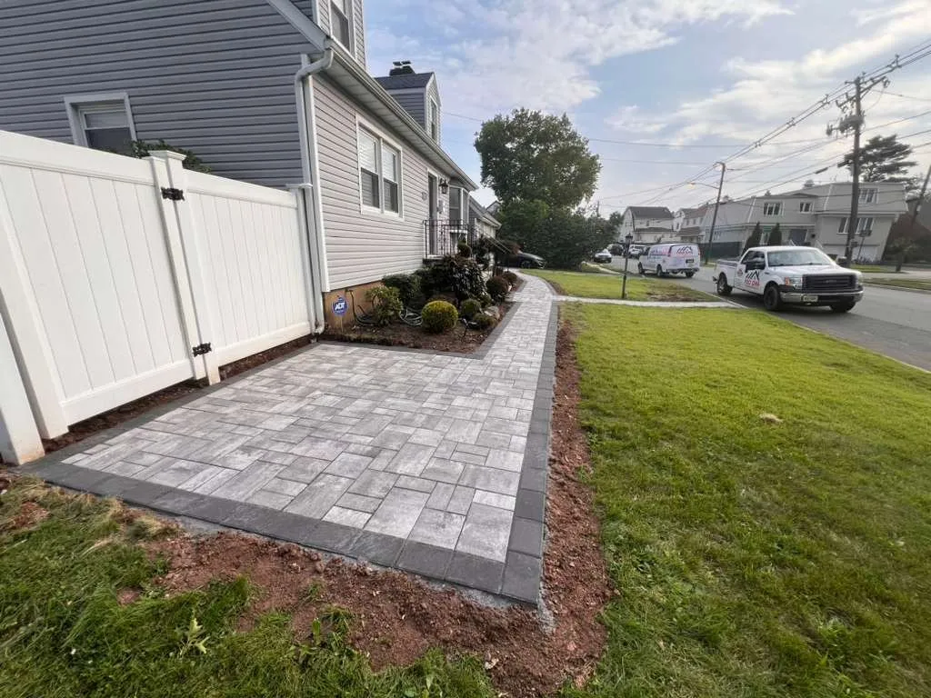 Gray paver walkway with a charcoal border along a white vinyl fence