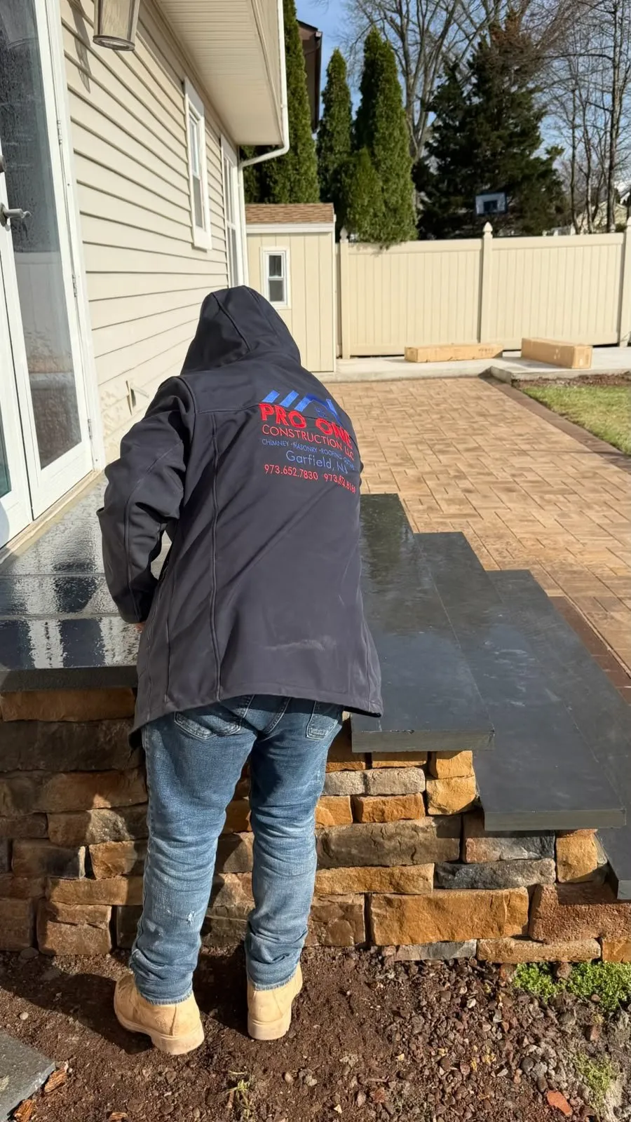Mason building stacked stone steps at the edge of a paver patio