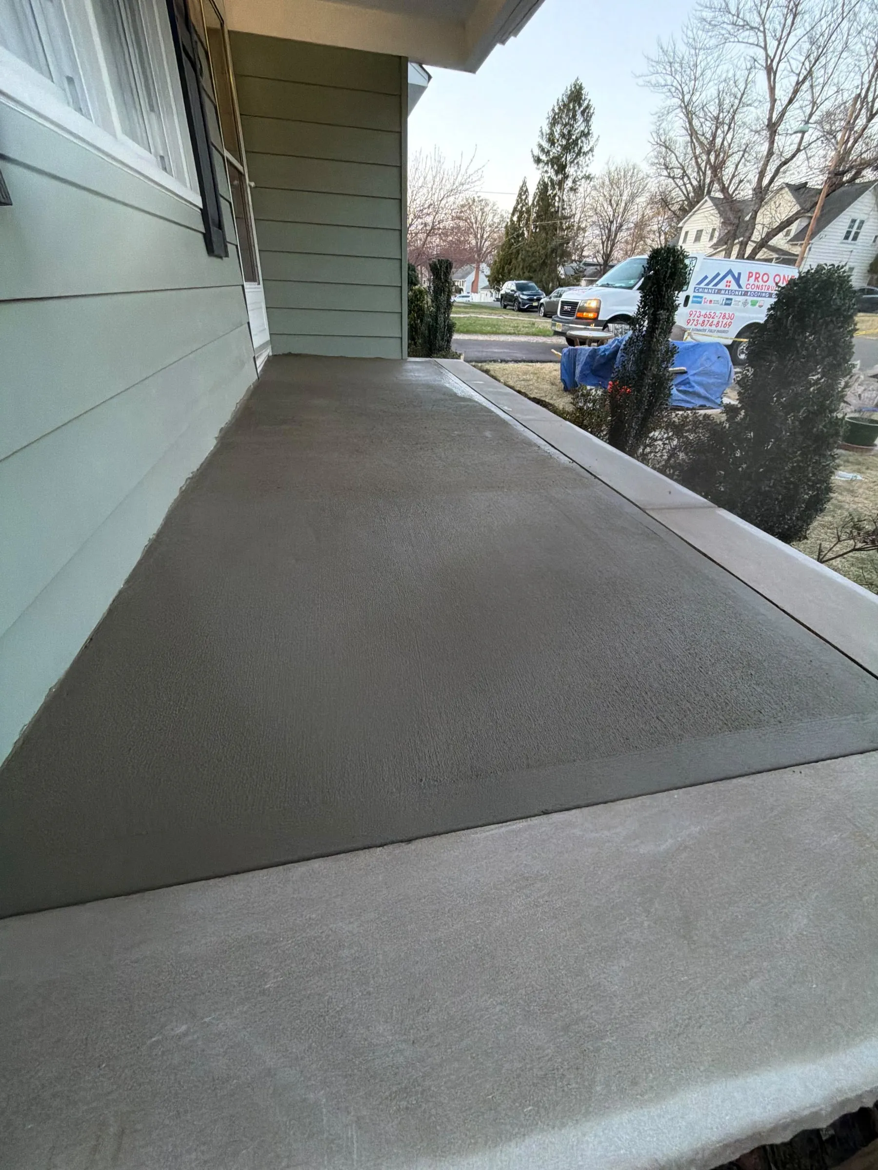 Freshly finished concrete front porch slab along a green sided home