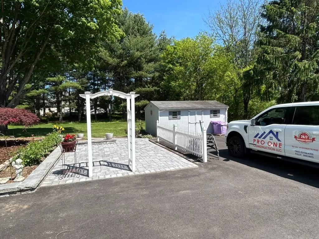 Gray paver patio with a white arbor beside the driveway