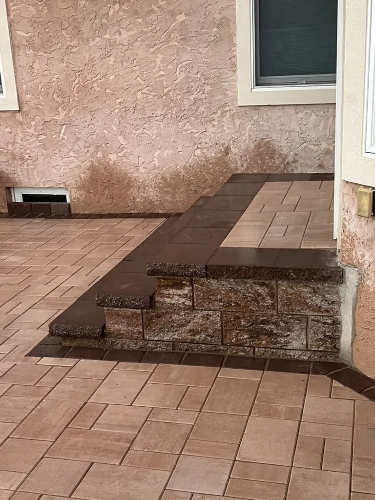 Wraparound paver step with a stone face along a stucco home