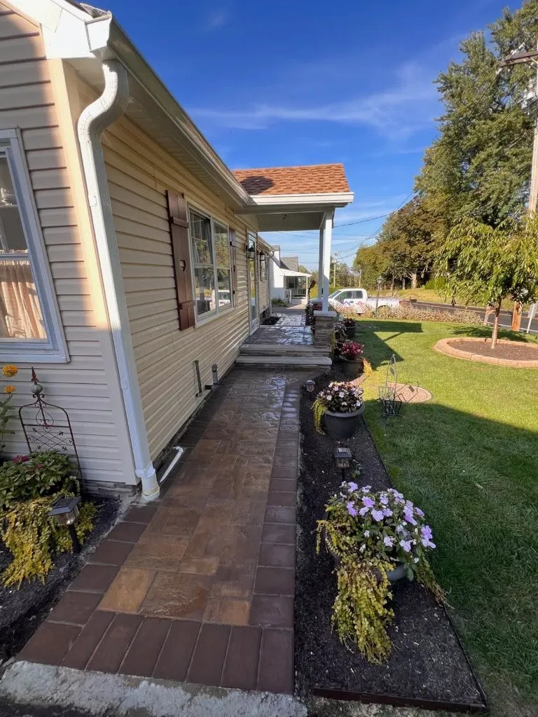 Paver walkway with dark border along a home, lined with flower beds