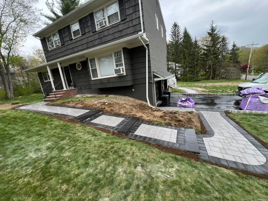 Gray paver walkway with charcoal borders wrapping around a dark colonial home