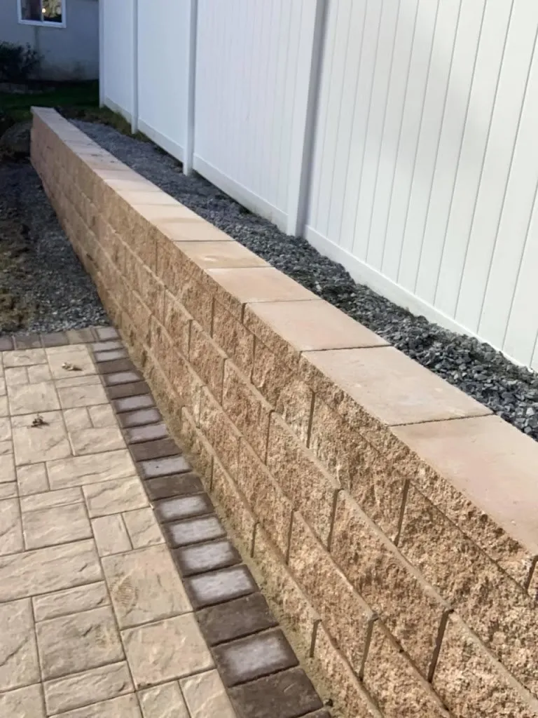 Segmental block retaining wall with a cap running along a paver walkway