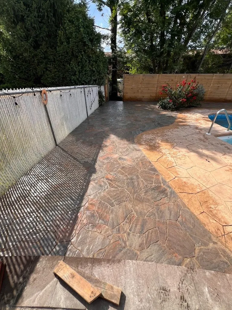 Stamped concrete pool deck being finished next to an in-ground pool
