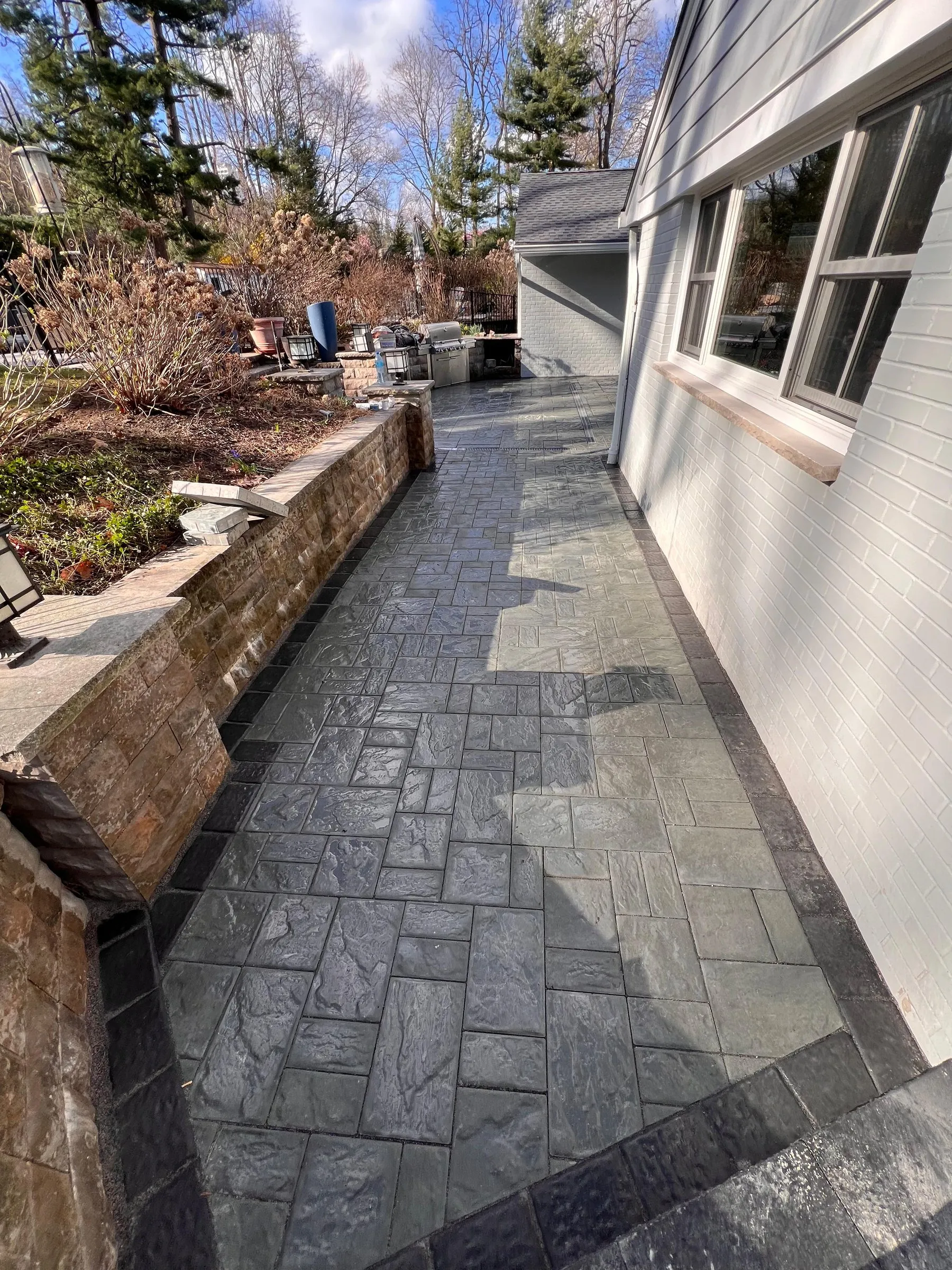 Slate-gray stamped concrete side walkway along a stone garden wall